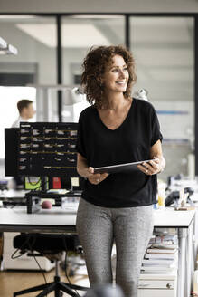 Businesswoman with digital tablet looking away while standing at office - PESF02465