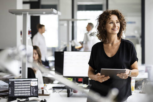 Smiling entrepreneur looking away while standing with colleague in background at open plan office - PESF02474