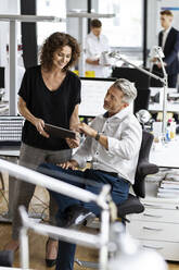 Geschäftsmann und Frau arbeiten an einem digitalen Tablet mit Kollegen im Hintergrund in einem Großraumbüro - PESF02481