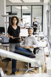 Selbstbewusste Geschäftsfrau, die neben einem Geschäftsmann steht, mit Kollegen im Hintergrund in einem Großraumbüro - PESF02482