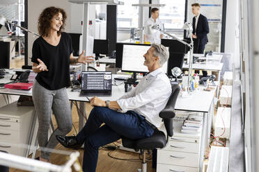 Smiling entrepreneurs discussing while working with colleagues in background at open plan office - PESF02483