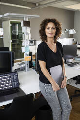 Unternehmerin mit digitalem Tablet, das sich im Stehen auf den Schreibtisch stützt - PESF02491