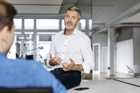 Mature businessman discussing with colleague while sitting at office - PESF02495