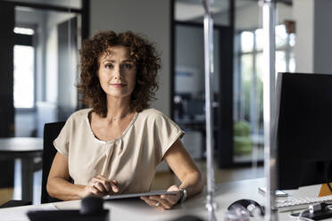 Selbstbewusste Geschäftsfrau, die ein digitales Tablet benutzt, während sie im Büro sitzt - PESF02504