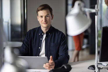 Confident young businessman using digital tablet while sitting at office - PESF02508