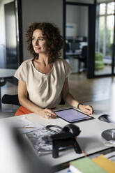 Businesswoman with digital tablet looking away while sitting at desk in office - PESF02513