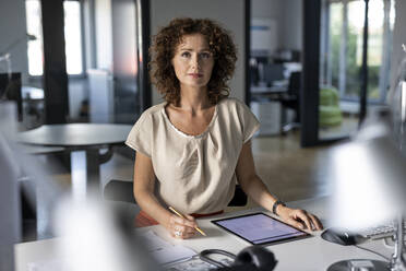 Selbstbewusste Geschäftsfrau mit digitalem Tablet, die am Schreibtisch im Büro sitzt - PESF02514