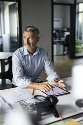 Businessman with digital tablet looking away while using digital tablet at office - PESF02515