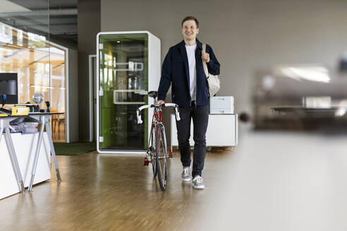 Young businessman holding bag while walking with bicycle at office - PESF02522