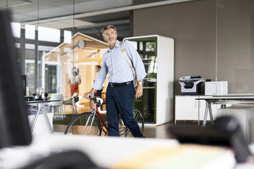 Mature businessman with bag and bicycle leaving after work from office - PESF02525