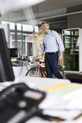 Businessman with bicycle and bag looking away while walking at office - PESF02526