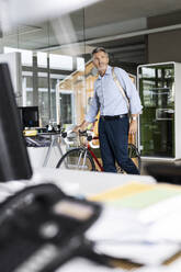 Geschäftsmann mit Fahrrad und Tasche schaut beim Gehen im Büro weg - PESF02526