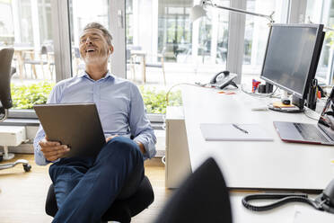 Lächelnder Unternehmer, der ein digitales Tablet benutzt, während er im Büro sitzt - PESF02534