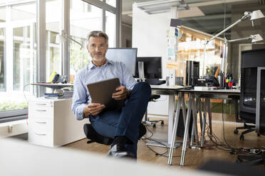 Selbstbewusster Unternehmer mit digitalem Tablet in einem Großraumbüro - PESF02535
