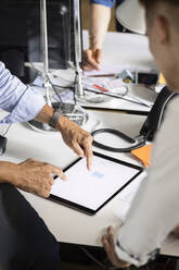 Geschäftsmann, der auf ein digitales Tablet zeigt, während er mit einem Kollegen im Büro arbeitet - PESF02538