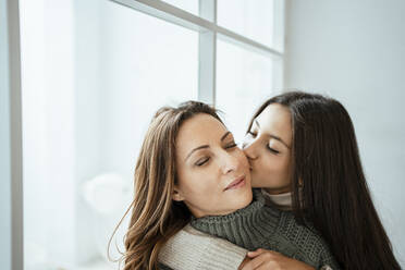 Tochter küsst Mutter auf die Wange am Fenster zu Hause - RCPF00636
