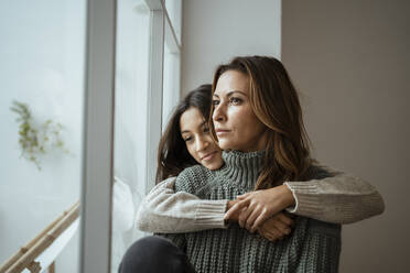 Daughter embracing mother while contemplating by window at home - RCPF00640