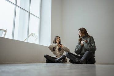 Daughter gesturing heart shape to mother while sitting together against wall at home - RCPF00652