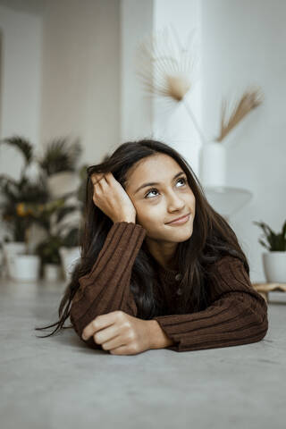 Smiling girl with head in hands contemplating while lying on front at home stock photo