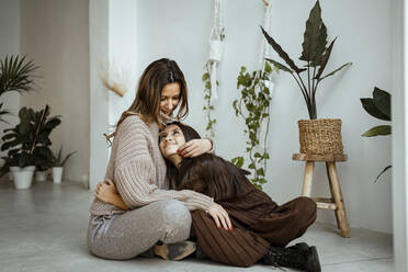 Smiling mother and daughter looking at each other while sitting on floor at home - RCPF00670