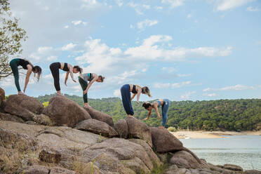 Junge Frauen mit Lehrerin üben Yoga auf einem Felsen - MRRF00793