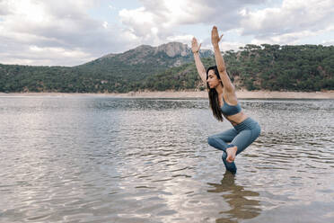 Young woman practicing yoga in lake - MRRF00816