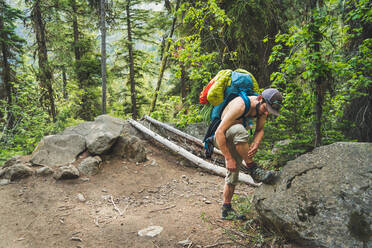 Shirtless man adjusts shoe on backpacking trip in Washington - CAVF91734