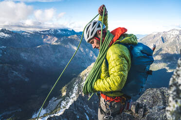 Mann mit Jacke und Rucksack wickelt Seil beim Klettern - CAVF91741