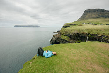 Woman with binoculars resting on grassy cliff - CAVF91769