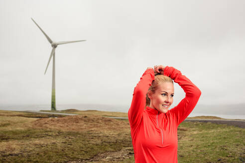 Weibliche Athletin beim Frisieren in der Nähe einer Windmühle - CAVF91775