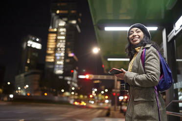 Lächelnde Frau, die nachts auf der Straße steht und sein Handy benutzt - CAVF91794