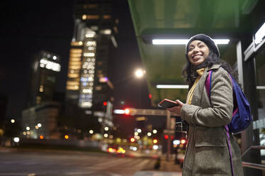 Smiling woman standing using his cellphone in the street at night - CAVF91794