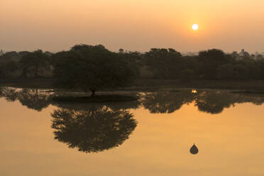 Bäume und Heißluftballon spiegeln sich bei Sonnenaufgang auf dem See, Bagan, Myanmar - CAVF91803