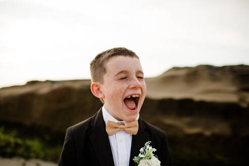 Neun Jahre alter Junge im Smoking lachend und stehend am Strand in San Diego - CAVF91810