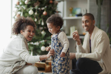 Glückliche Eltern und ihre kleine Tochter beim Schmücken des Weihnachtsbaums - CAIF30109