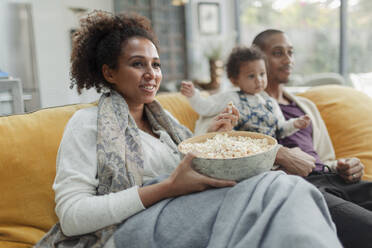 Glückliche Familie schaut einen Film und isst Popcorn auf dem Sofa im Wohnzimmer - CAIF30120