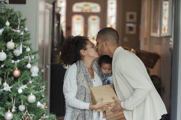 Verliebtes Paar mit kleiner Tochter küsst sich am Weihnachtsbaum - CAIF30126