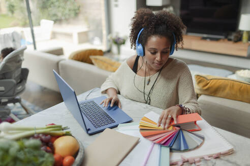 Designerin mit Farbmustern bei der Arbeit von zu Hause am Laptop - CAIF30143