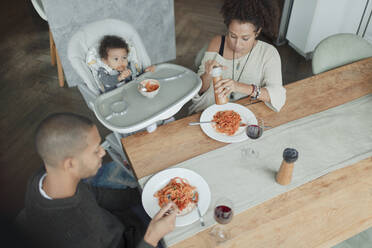 Familie isst Spaghetti am Esstisch und im Hochstuhl - CAIF30144