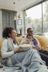 Familie schaut einen Film und isst Popcorn auf dem Wohnzimmersofa - CAIF30152