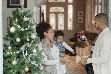 Glückliche Familie mit Weihnachtsgeschenken unter dem Baum im Wohnzimmer - CAIF30158