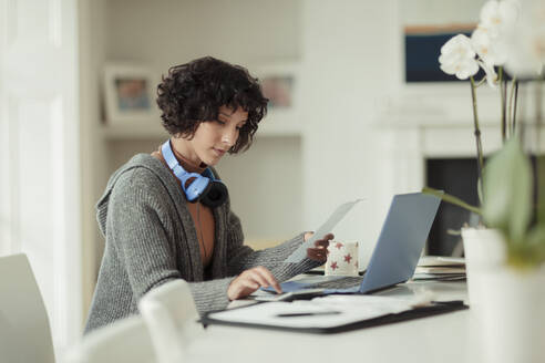 Frau arbeitet von zu Hause aus am Laptop auf dem Esstisch - CAIF30177