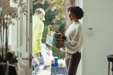 Woman receiving grocery delivery from courier at front door - CAIF30191