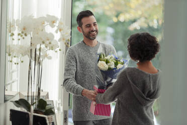 Glücklicher Ehemann überrascht Frau mit Blumen an der Haustür - CAIF30196