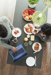 Ehepaar genießt das Frühstück und arbeitet am Laptop in der morgendlichen Küche - CAIF30198