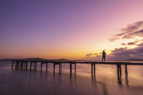 Silhouette einer Frau, die in der Morgendämmerung allein auf einem Steg an der Küste steht - FOF11933