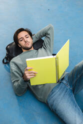 Young man studying while lying on backpack at basketball court - JMPF00784