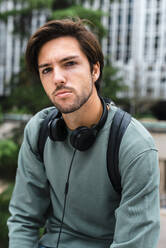 Hübscher junger Student mit Kopfhörern auf dem Campus - JMPF00788