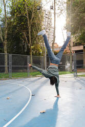 Mann mit Handstand bei akrobatischer Aktivität auf dem Basketballplatz auf dem Campus im Herbst - JMPF00791