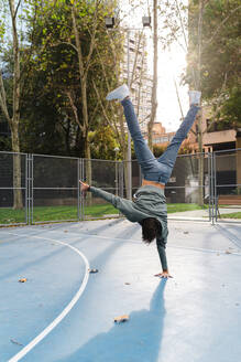 Man with handstand doing acrobatic activity at basketball court in campus during autumn - JMPF00791